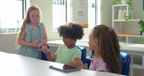 Children collaborating on rebus riddle in bright classroom using tablet for teamwork