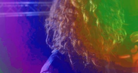 Curly-Haired Singer Performing Under Neon Purple and Green Stage Lights