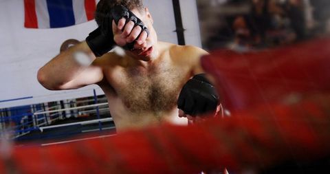 Shirtless boxer wiping sweat after intense round in gym ring with red ropes
