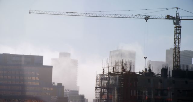 A construction site with a crane towers over emerging buildings amidst a hazy skyline, with copy space. The misty atmosphere adds a sense of mystery and scale to the urban development in progress.