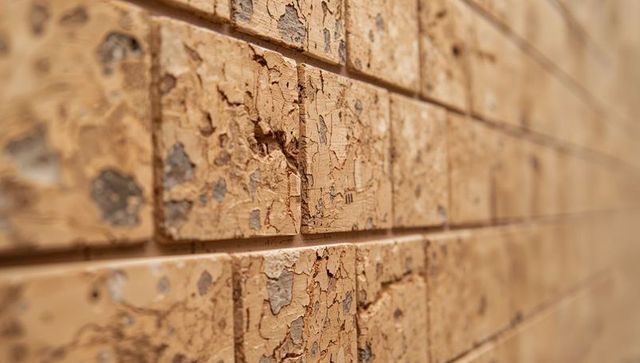 Peeling beige brick wall flaking paint revealing gray undercoat textured masonry closeup