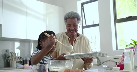 Senior woman and young girl pouring batter into muffin tin while baking together at home