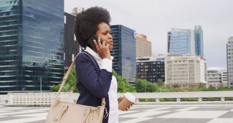 Confident Businesswoman Walking in City with Coffee and Smartphone