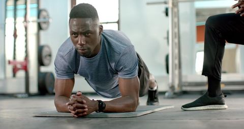 African American Man Holding Forearm Plank While Trainer Observing in Gym Fitness Session