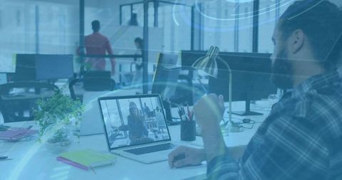 Bearded man pointing at laptop during video conference in modern coworking office