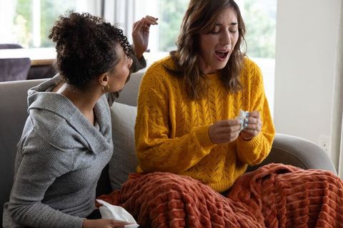 Black friend comforting white friend on couch, holding medication blister, cozy home scene