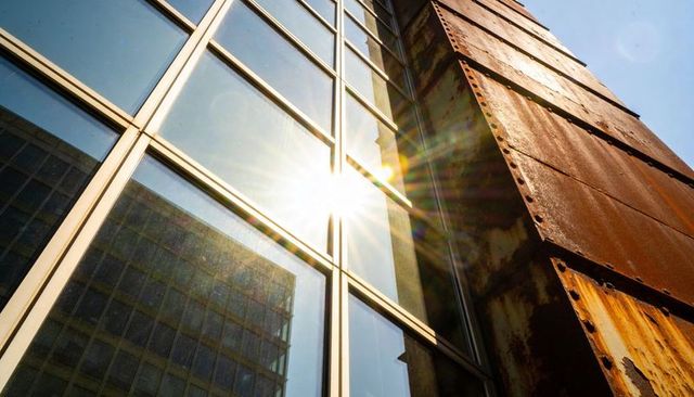 Sunburst hitting glass curtain wall and rusted steel facade showing urban contrast