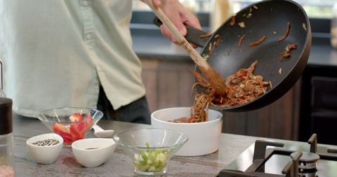 Chef Pouring Tasty Stir-Fried Noodles from Wok in Modern Kitchen