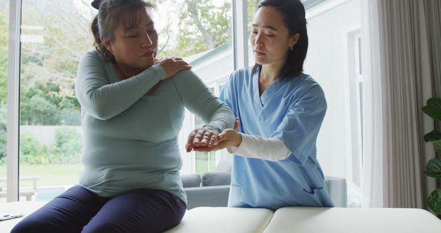 Asian female physiotherapist treating female patient at surgery, moving her arm. physiotherapy, health and healthcare services.