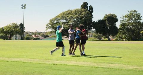 Teens celebrating victory on sports field embracing in group hug showing team unity