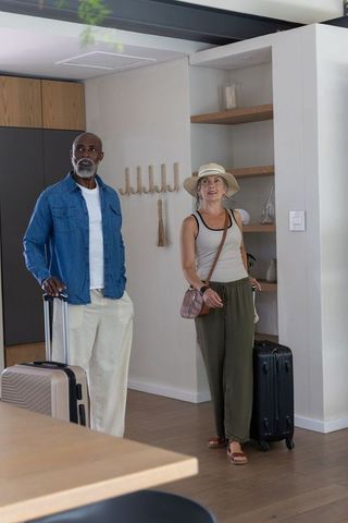 Mixed-age couple arriving at modern apartment foyer holding suitcases and looking around