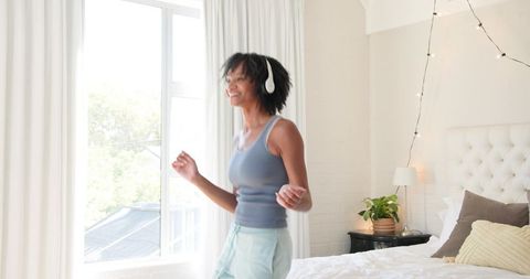 Woman Dancing Joyfully with Headphones in Cozy Sunlit Bedroom
