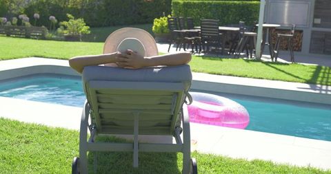 African american woman reclining on poolside lounge chair with sunhat and pink pool float