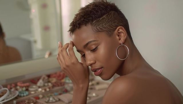 Contemplative woman tilting head at vanity wearing silver hoop earrings and stacked jewelry