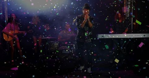Dynamic live band performing on confetti-filled stage with lead singer gripping microphone