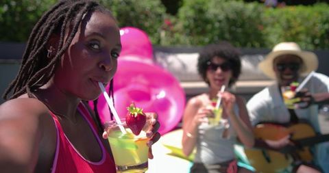 African american friends sipping cocktails poolside with guitar and pink float