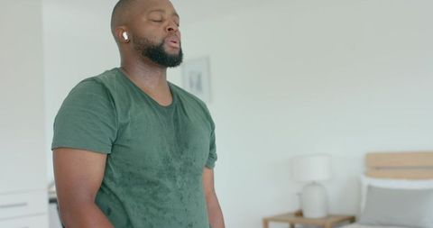 Catching breath after intense home workout wearing wet green t-shirt and earbuds