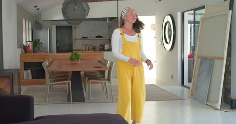 Mature woman walking through modern minimalist home wearing yellow overalls