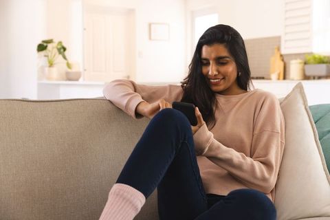 Woman Relaxing on Sofa While Using Smartphone in Cozy Living Room