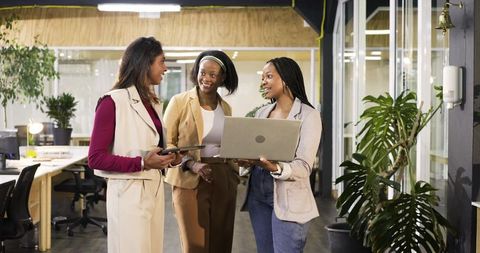 Multicultural female team collaborating in modern open-plan office with laptop and tablet