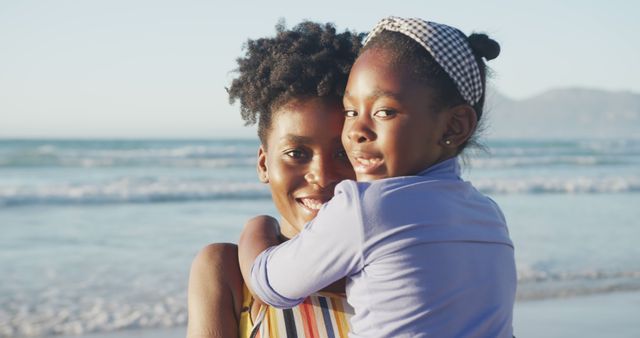 Portrait of happy african american mother embracing daughter on sunny beach. healthy and active time beach holiday.