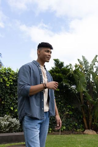 Young african american man standing in backyard garden wearing denim shirt and bracelets