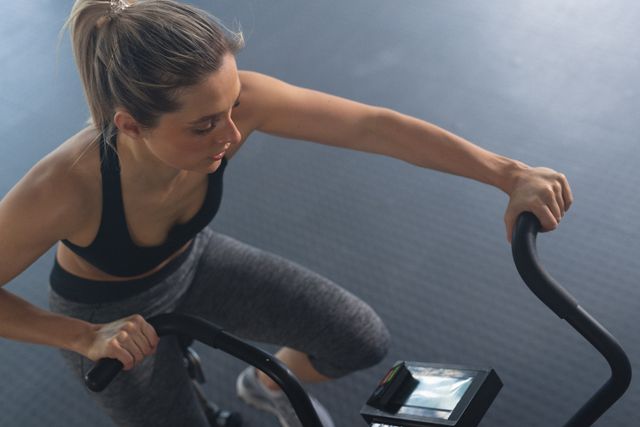 Caucasian woman using a stationary bike in a gym, focusing on her workout. Ideal for promoting fitness, health, and active lifestyle concepts. Suitable for use in fitness blogs, gym advertisements, health and wellness articles, and sports equipment promotions.