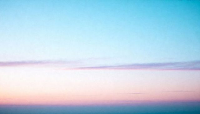 Glowing pastel dawn sky showing soft gradient and thin cloud band over calm horizon
