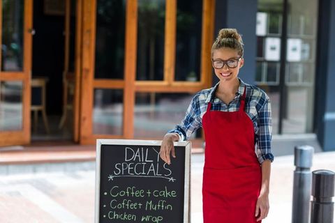 Cheerful Cafe Worker with Daily Specials Chalkboard Outside Cafe