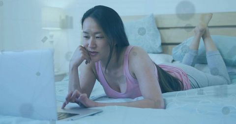 Asian Woman Engaged in Online Activity from Cozy Bedroom