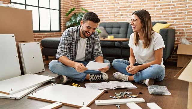 Happy couple assembling flatpack furniture in modern loft living room, unpacking joy