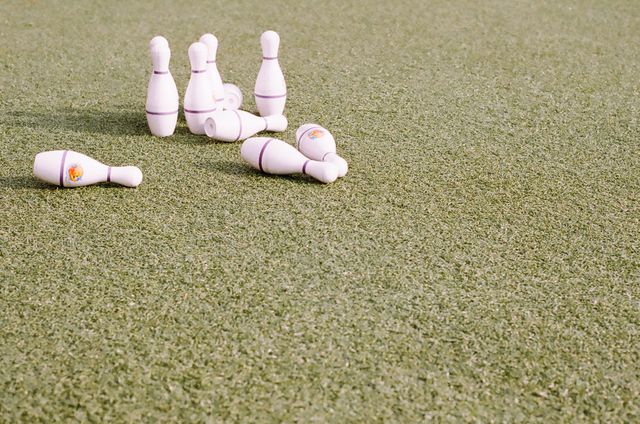 White bowling pins are scattered across a green grass lawn. Perfect for illustrating outdoor games, casual recreation activities, summer gatherings, and family fun events.