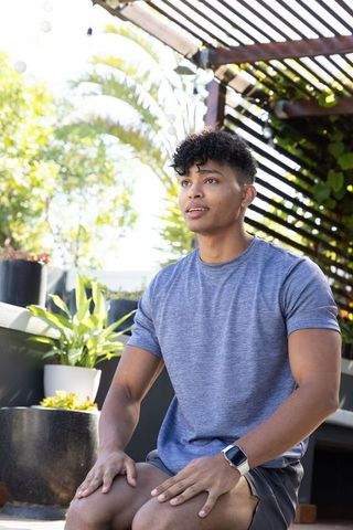 Sunlit rooftop portrait of african american man sitting on terrace wearing smartwatch