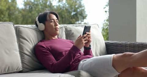 Relaxed Young Man with Headphones Using Smartphone on Patio