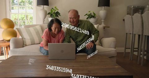 Mature couple browsing laptop together in cozy living room with floating numeric data