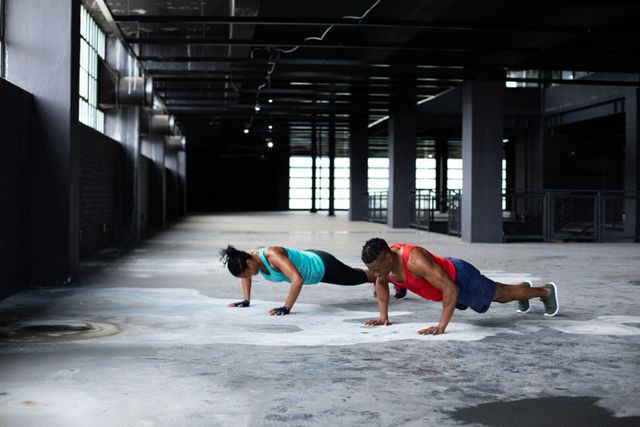 African American man and woman performing push ups in an empty building. Ideal for promoting fitness, healthy lifestyle, urban workout routines, and strength training programs. Suitable for use in fitness blogs, gym advertisements, and health-related articles.