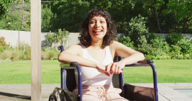 Woman sitting in wheelchair outdoors on a sunny day, smiling and enjoying the garden setting. The greenery and bright sunlight create a refreshing and positive atmosphere. This image is perfect for use in articles and campaigns promoting diversity, inclusion, wellness, and empowerment of individuals with disabilities. Ideal for healthcare, wellness blogs, lifestyle websites, and inclusive ad campaigns.