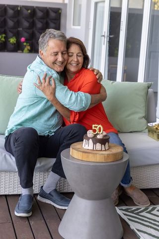 Senior couple celebrating 50th anniversary with chocolate cake and warm embrace on patio