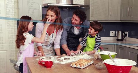 Parents and kids laughing while baking on kitchen island with flour, eggs and rolling pin