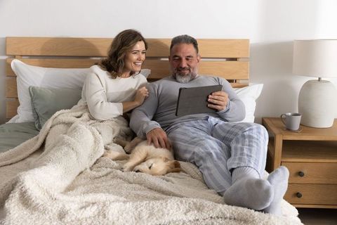 Middle-aged couple relaxing in bed watching tablet and petting sleeping puppy