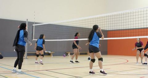 Diverse girls volleyball teams competing indoors on gym court wearing hijab and knee pads