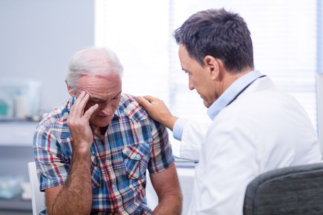 Senior man sitting in clinic, looking distressed, while doctor offers support by placing hand on shoulder. Ideal for illustrating healthcare services, elderly care, and compassionate medical support.