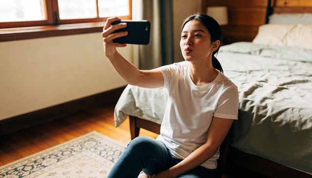 Taking selfie puckering lips on sunlit bedroom floor casual white tee and jeans