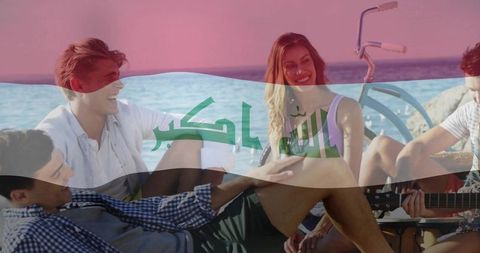 Young friends playing guitar on beach with iraqi flag overlay, summer coastal leisure