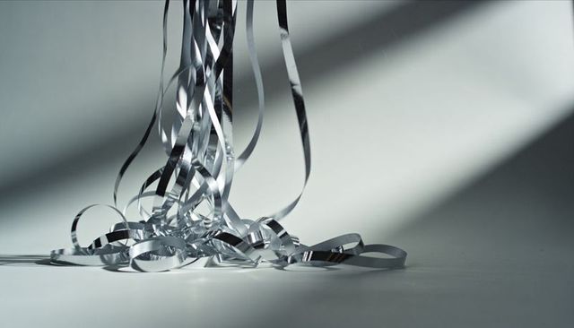Minimalist metallic silver curling ribbons falling with diagonal shadows on pale gray surface