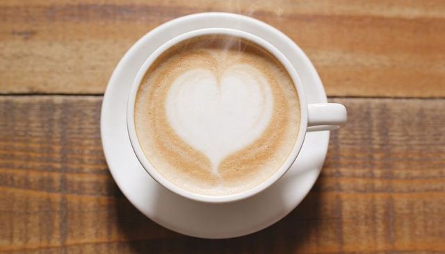 Steaming latte with heart foam in white cup on rustic wooden table