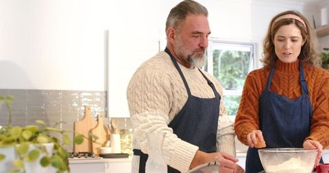 Couple baking together in sunlit kitchen preparing batter with egg and flour