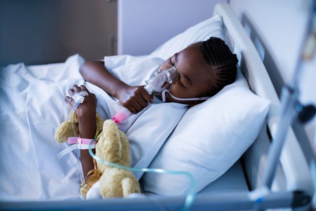 Child is lying in hospital bed, wearing oxygen mask and sleeping. The child is holding a teddy bear, creating a comforting and caring atmosphere. Intravenous line is visible, indicating medical treatment. Ideal for topics related to pediatric healthcare, recovery, illness, and medical care for children.