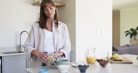 Caucasian Woman Pouring Cereal in Modern Kitchen Surround by Healthy Breakfast Items