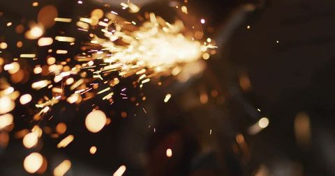 Orange sparks streaming across dark workshop, ember streaks and industrial bokeh motion